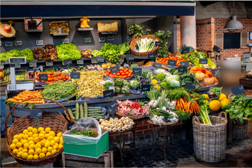 Vegetable market with various fresh produce displayed on tables and shelves.